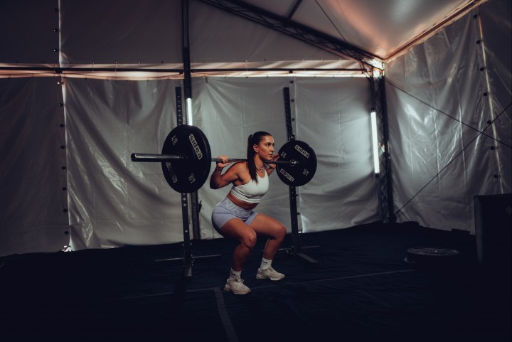 Athlete performing a barbell back squat in a tent gym