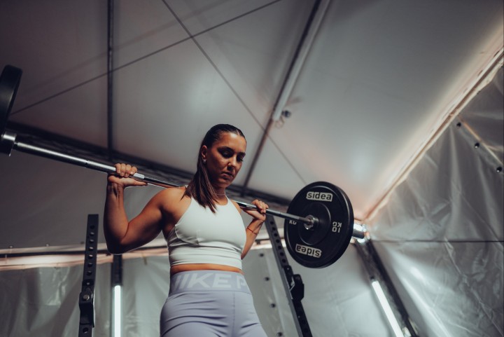 Athlete with a barbell on her shoulders in a weight room, shot from below