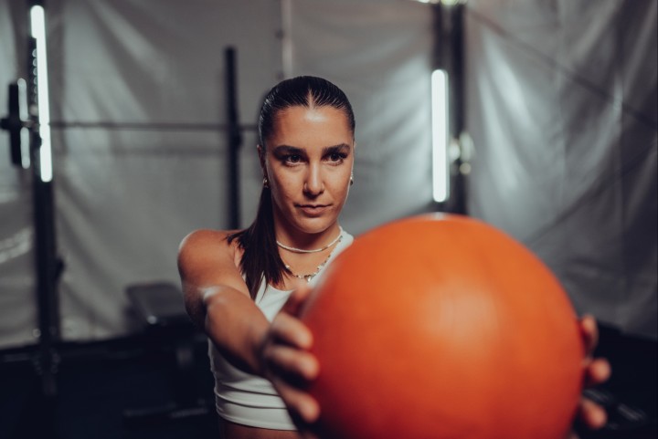 Atleta tiene una palla medica a braccia tese davanti a sé, in una palestra sotto una tenda