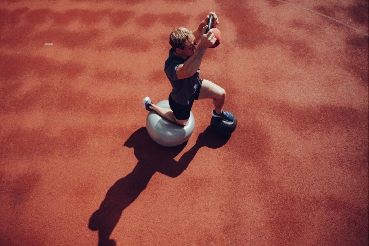 Athlete kneeling on a stability ball holding a medicine ball overhead, shot from above