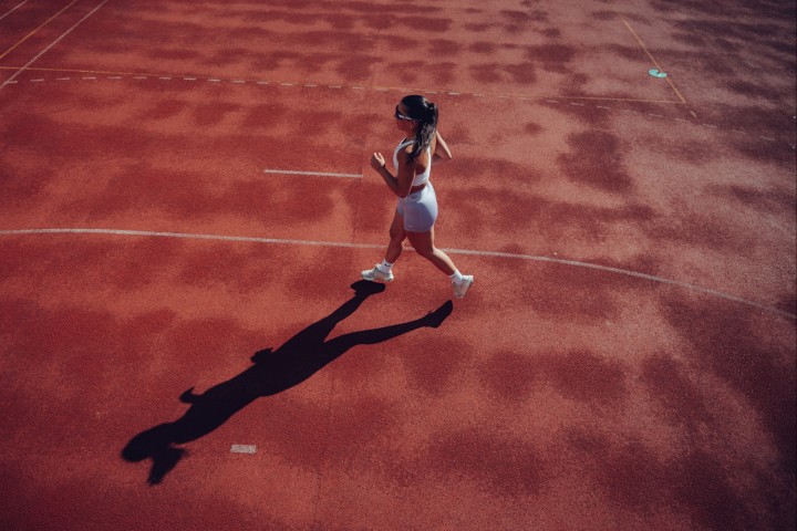 Athlete running on the red track, photographed from above, casting a long shadow