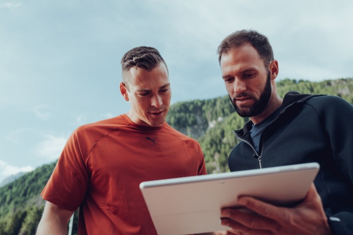 Coach and athlete looking at a tablet together, with wooded mountains in the background